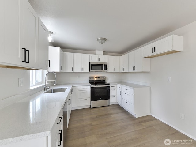 kitchen featuring light stone countertops, light wood-type flooring, white cabinets, stainless steel appliances, and a sink