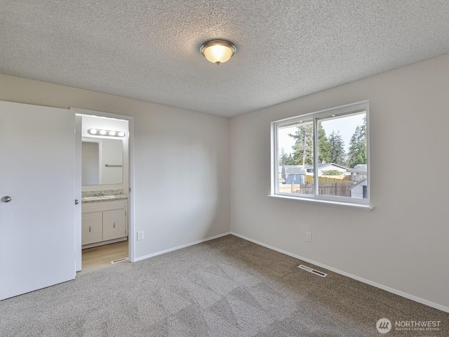 unfurnished bedroom with visible vents, baseboards, carpet floors, ensuite bathroom, and a textured ceiling