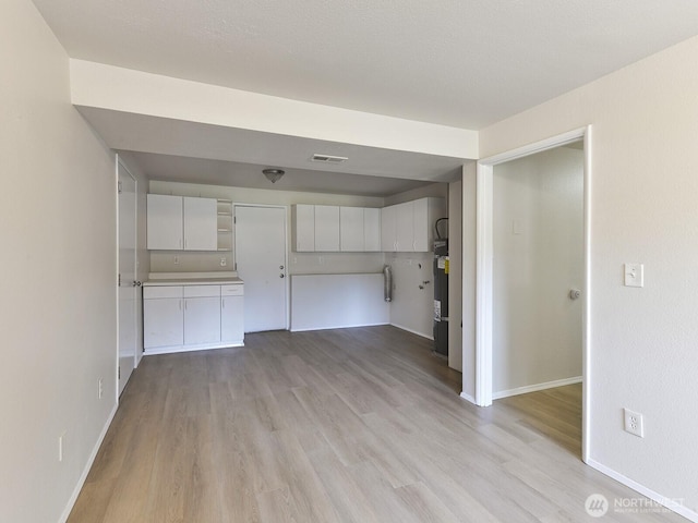 unfurnished living room with visible vents, light wood-type flooring, and baseboards