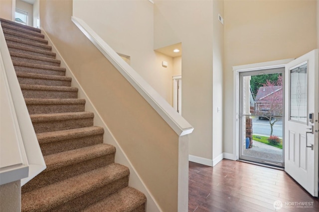foyer featuring stairway, baseboards, dark wood-style flooring, and a towering ceiling