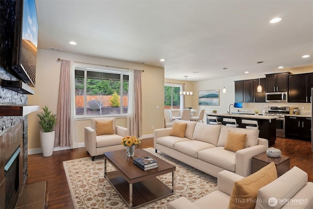 living room featuring a stone fireplace, visible vents, recessed lighting, and dark wood-style flooring