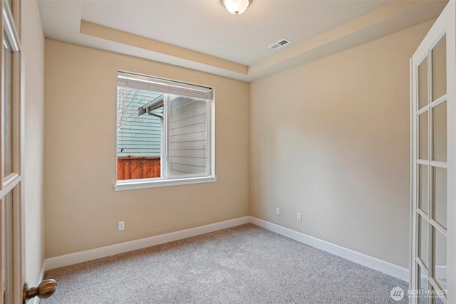 carpeted empty room with visible vents, a healthy amount of sunlight, a tray ceiling, and baseboards