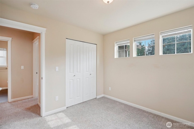 unfurnished bedroom with a closet, carpet flooring, multiple windows, and baseboards