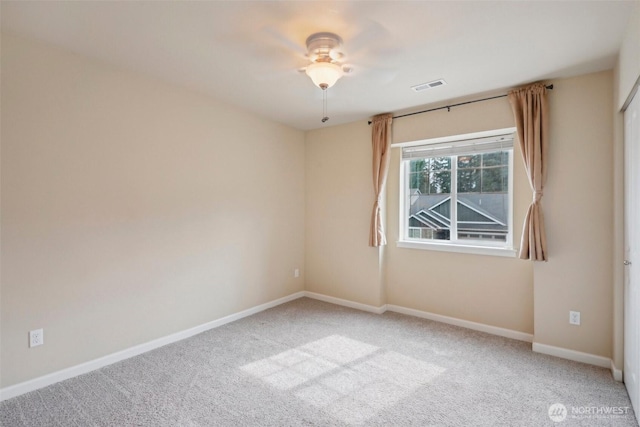 carpeted spare room featuring baseboards, visible vents, and ceiling fan