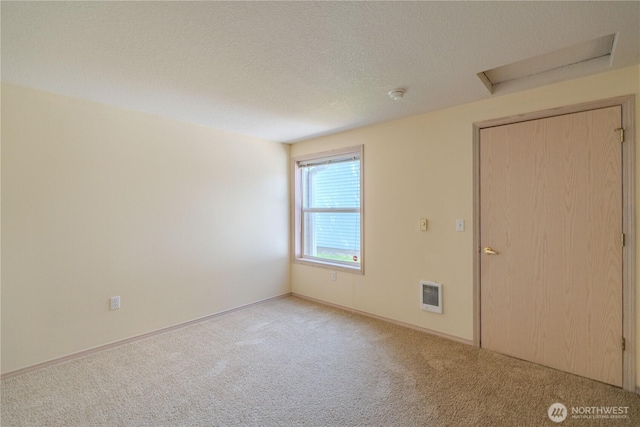 carpeted spare room with attic access, heating unit, baseboards, and a textured ceiling