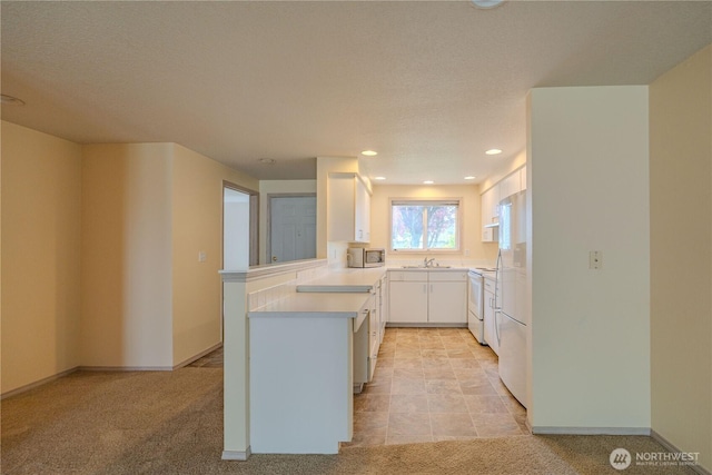 kitchen with stainless steel microwave, a sink, a peninsula, light countertops, and white cabinets