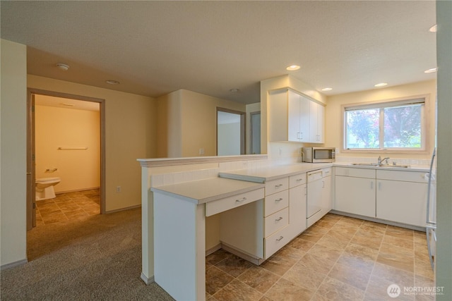 kitchen with stainless steel microwave, a peninsula, white cabinetry, light countertops, and dishwasher