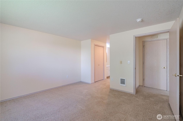 empty room featuring a textured ceiling, visible vents, baseboards, and light carpet