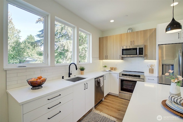 kitchen with a sink, light countertops, appliances with stainless steel finishes, decorative light fixtures, and tasteful backsplash