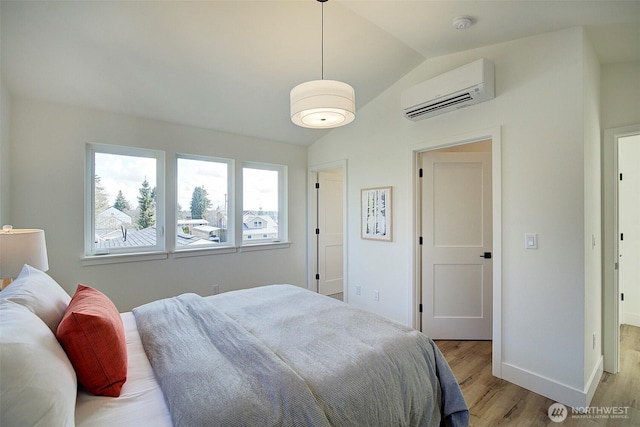 bedroom with a wall unit AC, baseboards, light wood-type flooring, and vaulted ceiling
