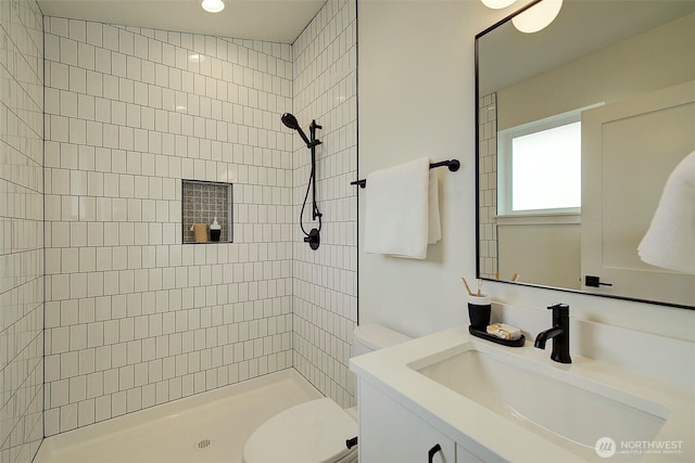bathroom featuring tiled shower, toilet, and vanity