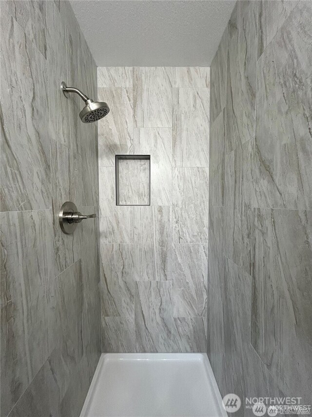 bathroom with a textured ceiling and tiled shower