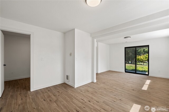 empty room with visible vents, light wood-style flooring, and baseboards