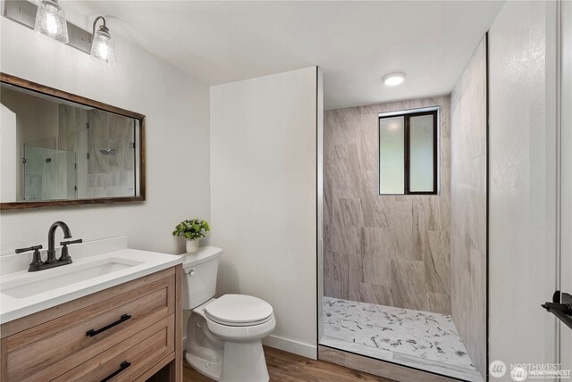 bathroom featuring a tile shower, vanity, toilet, baseboards, and wood finished floors