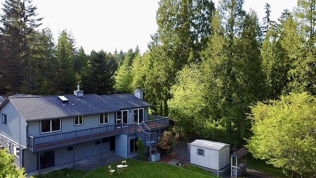 rear view of house with an outbuilding, a wooden deck, a shed, a yard, and a shingled roof