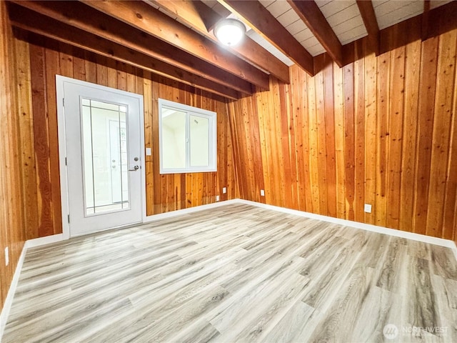 unfurnished room with wooden walls, wood finished floors, and beam ceiling