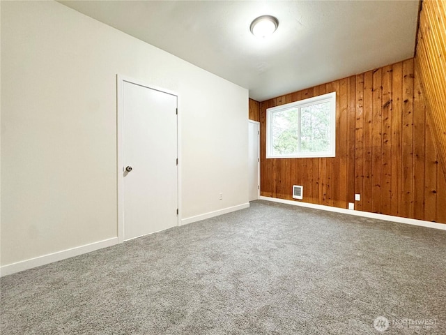 carpeted spare room with baseboards and wood walls