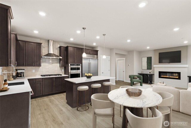 10591 135th Ave NE Unit 24, Kirkland, WA 98033 - kitchen featuring wall chimney exhaust hood, appliances with stainless steel finishes, open floor plan, dark brown cabinets, and a kitchen island