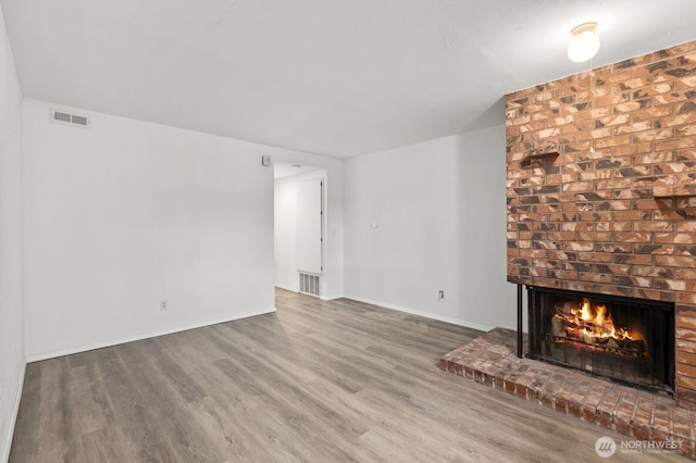 unfurnished living room featuring baseboards, a brick fireplace, wood finished floors, and visible vents