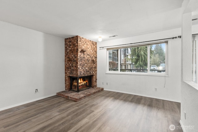 unfurnished living room featuring baseboards, wood finished floors, visible vents, and a fireplace
