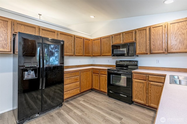 kitchen featuring brown cabinets, light countertops, black appliances, lofted ceiling, and light wood-style flooring