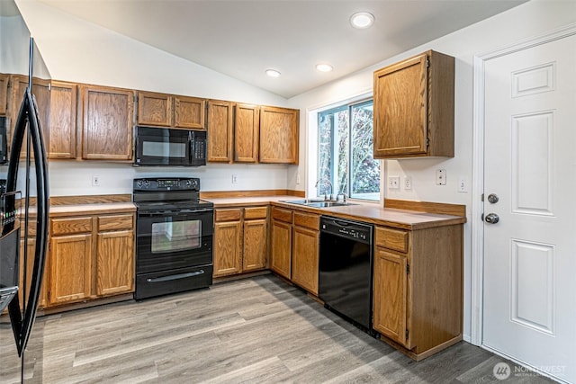 kitchen featuring light wood-type flooring, recessed lighting, a sink, black appliances, and vaulted ceiling
