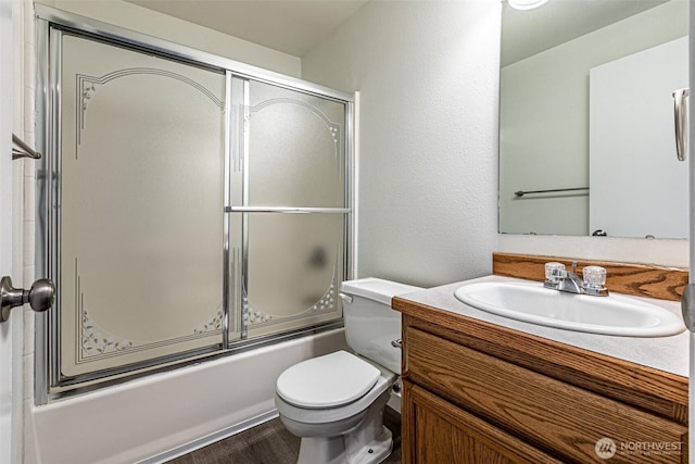 bathroom featuring vanity, bath / shower combo with glass door, wood finished floors, and toilet