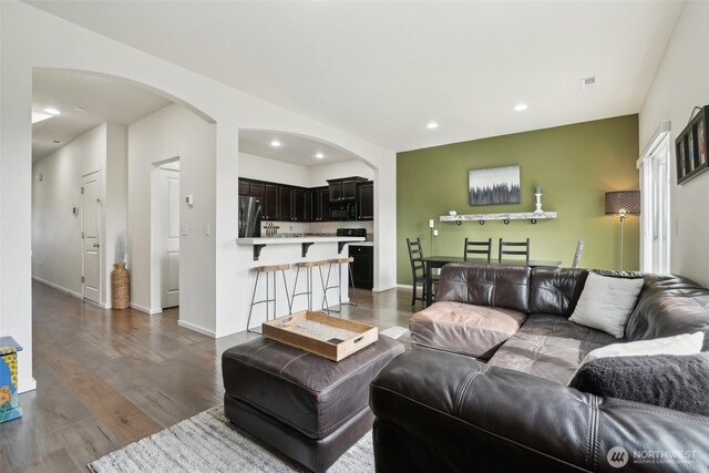 living room with visible vents, arched walkways, dark wood finished floors, baseboards, and recessed lighting