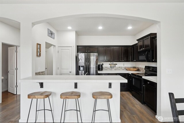 kitchen with a breakfast bar area, arched walkways, dark wood finished floors, and black appliances