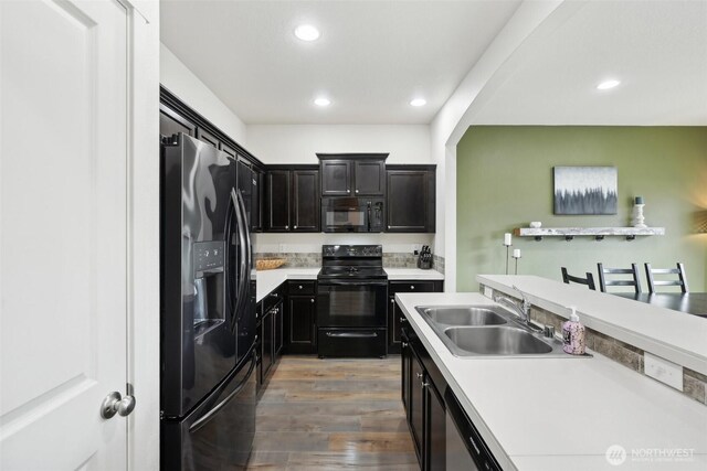 kitchen with wood finished floors, recessed lighting, light countertops, a sink, and black appliances