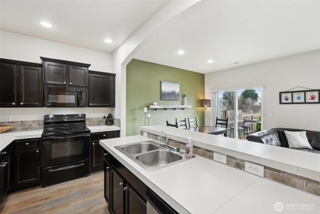 kitchen with a sink, light countertops, black appliances, light wood-style floors, and recessed lighting