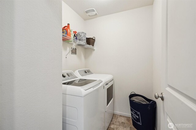 clothes washing area featuring baseboards, laundry area, washing machine and dryer, and stone finish floor