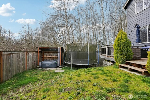 view of yard featuring a wooden deck, a fenced backyard, and a trampoline