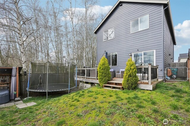 back of property with a yard, fence, a wooden deck, and a trampoline
