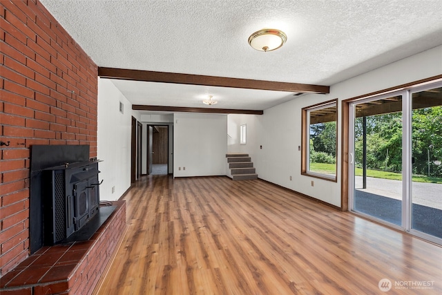 1918 SE Maple Dr, Chehalis, WA 98532 - unfurnished living room with a textured ceiling, wood finished floors, a wood stove, beamed ceiling, and stairway