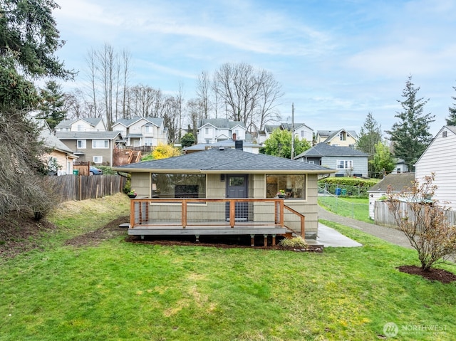 rear view of property featuring a residential view, a deck, fence, and a lawn