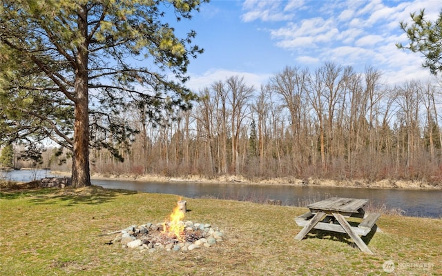 view of yard featuring a forest view, a water view, and a fire pit