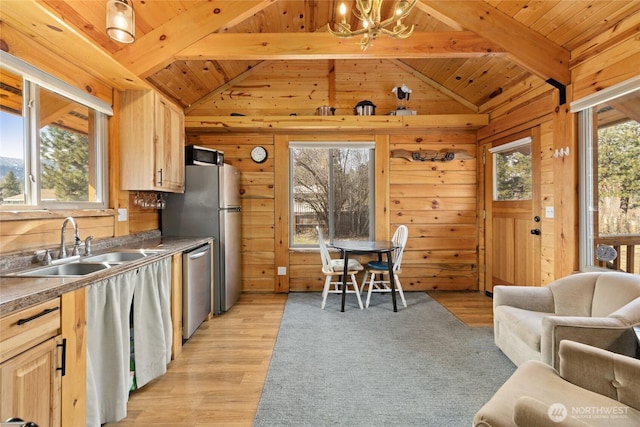 kitchen with vaulted ceiling with beams, a sink, wood walls, stainless steel dishwasher, and a notable chandelier