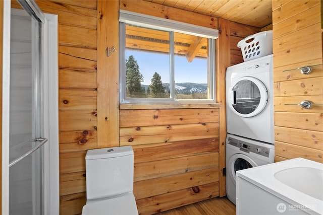 clothes washing area with wood ceiling, wood walls, stacked washing maching and dryer, and light wood-type flooring
