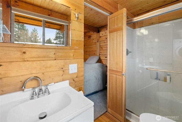 bathroom with a stall shower, wood walls, wooden ceiling, and a sink