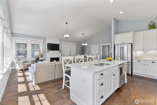 kitchen featuring a breakfast bar, dark wood finished floors, a warm lit fireplace, stainless steel appliances, and a sink