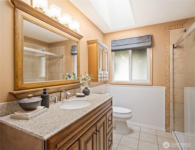 full bath with a skylight, tile patterned flooring, a shower stall, wainscoting, and toilet