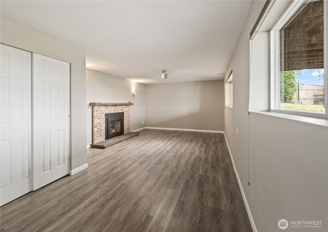 unfurnished living room with a brick fireplace, baseboards, and wood finished floors