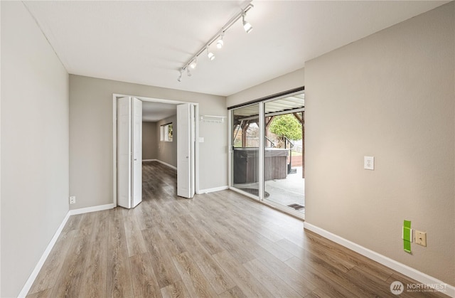 unfurnished room with baseboards, rail lighting, and light wood finished floors