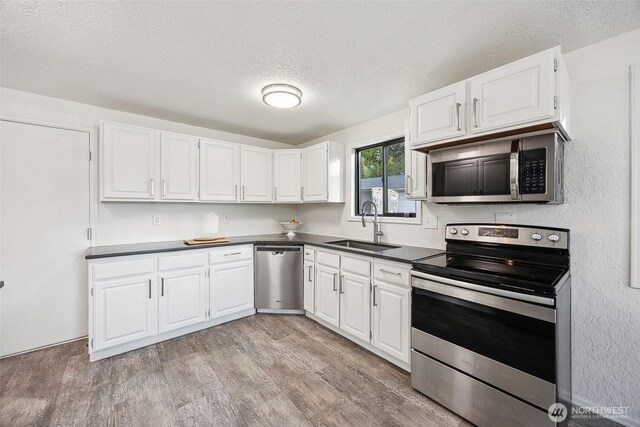 10231 Kiwa Dr SE, Olympia, WA 98513 - kitchen with a textured ceiling, a sink, dark countertops, white cabinets, and appliances with stainless steel finishes