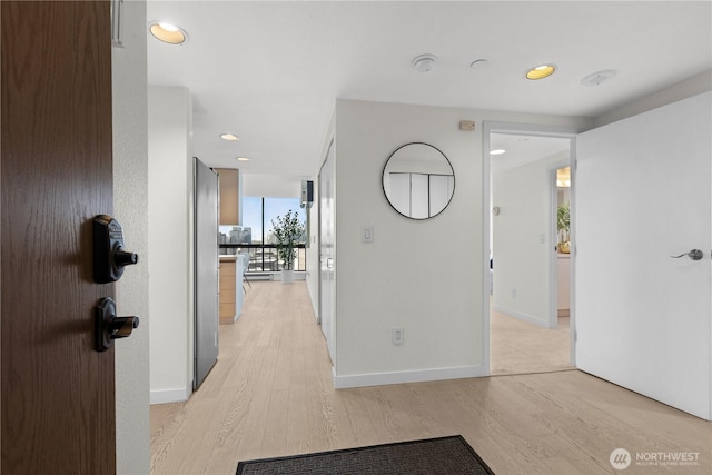 hallway featuring expansive windows, baseboards, light wood finished floors, and recessed lighting