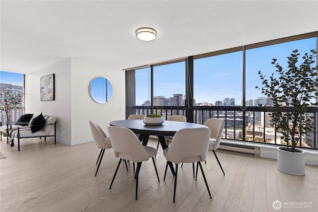 dining room with expansive windows, a view of city, wood finished floors, and a baseboard radiator