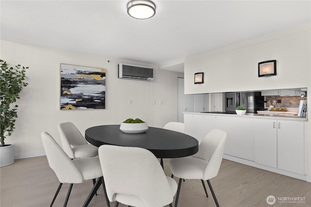 dining space featuring light wood finished floors, baseboards, and a wall mounted AC