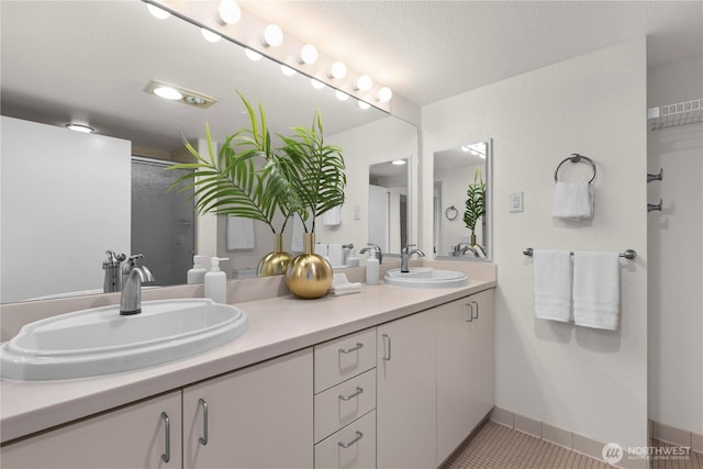 full bath featuring a shower with door, tile patterned floors, double vanity, and a sink