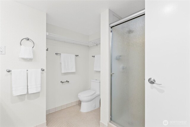 bathroom featuring tile patterned floors, toilet, a stall shower, and baseboards
